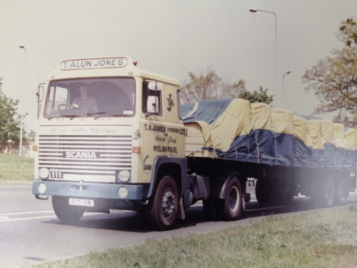 A scania lorry covered in blue and yellow T Alun Jones branded cover